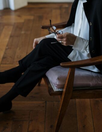 A woman holding glasses, seated indoors, exuding professionalism and calm.