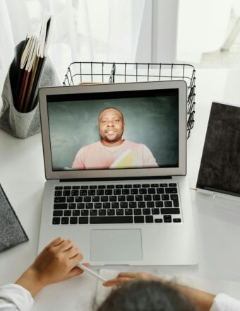A student participates in a virtual class with a teacher on a laptop screen.